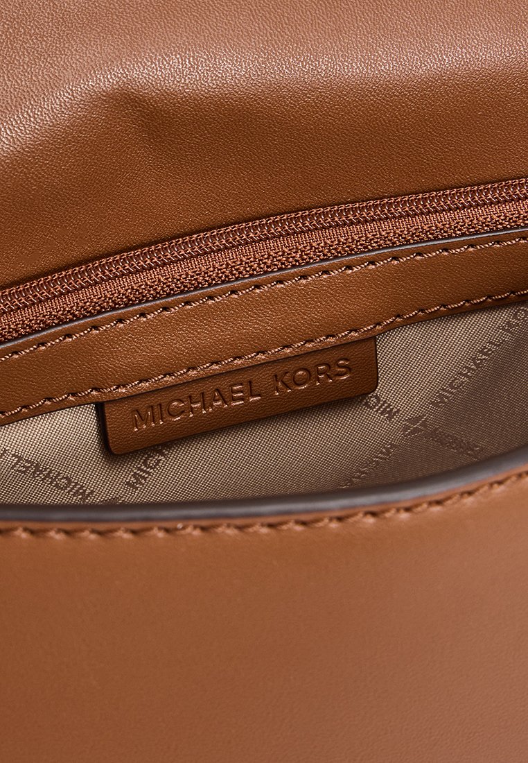 Innenansicht einer braunen Lederhandtasche mit einem Reißverschlussfach und einem Markenlabel. Glatte Textur mit dezenten Steppnähten.