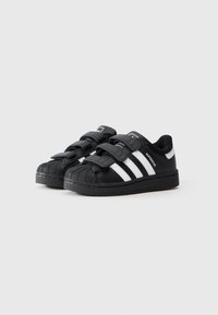 Schwarze Ledersneaker mit Gummisohle, ausgestattet mit einer strukturierten Zehenkappe, drei weißen Streifen und Klettverschlussriemen zum Schließen.
