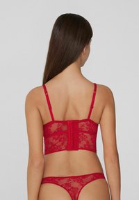 Czerwona koronkowa braletka z regulowanymi ramiączkami i zapięciem na haftki. Posiada kwiatowy wzór i przezroczystą strukturę, zestawiona z dopasowanym stringiem.