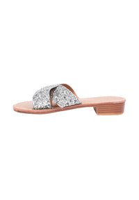 Le ciabatte glitterate argento presentano un design con cinturini incrociati, suola piatta e tacco basso, con una soletta e una base in pelle color cuoio.