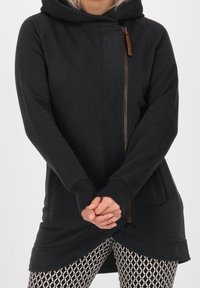 Sudadera con capucha negra, con cremallera frontal y bolsillos, que presenta un dobladillo curvado y puños acanalados. Textura suave, diseño casual.