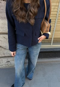 Jūros mėlynumo megztas švarkas su dviem priekiniais kišenėmis, derinamas su šviesiai mėlynomis platėjančiomis džinsinėmis kelnių. Taip pat turi šviesiai rudos spalvos pečių krepšį su užtrauktuku.