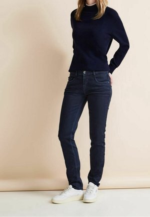 Dark blue jeans with a slim fit, paired with a navy sweater. The jeans feature classic five-pocket styling and a smooth texture. White sneakers.