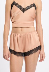 Satynowy komplet: koszulka na ramiączkach i szorty w delikatnym odcieniu brzoskwini, ozdobione czarną koronką na dekolcie i krawędziach, o luźnym kroju i elastycznej talii.