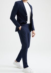 Navy kavaj och byxor med en texturerad yta, kombinerat med en vit t-shirt och vita sneakers. Skräddarsydd passform och tvåknappsöppning.