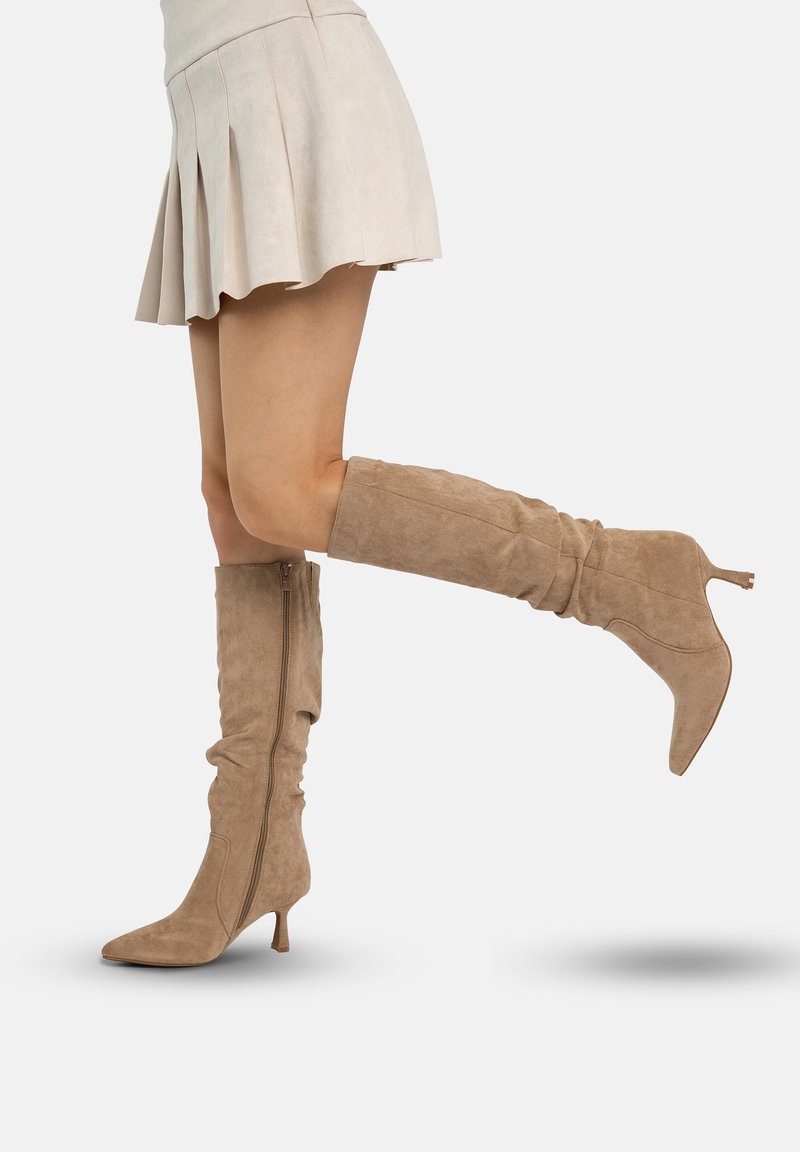 Beige suède laarzen tot aan de knie met een slouchontwerp en een spits toe. Voorzien van een ritssluiting aan de zijkant en een bescheiden stilettohak.