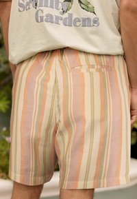 Pantalones cortos a rayas fabricados con un material ligero, que presentan rayas verticales en suaves colores pastel de melocotón, verde y beige; incluyen un bolsillo trasero.