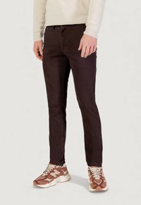 Pantaloni slim-fit marrone scuro in cotone, con una texture sottile, gambe dritte e tasche frontali, abbinati a sneaker marroni e crema.
