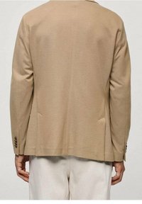 Blazer en laine beige avec une coupe cintrée, deux poches latérales et des poignets boutonnés, présentant une texture lisse et un design épuré et simple.