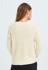 Maglione a maglia beige con finitura texturizzata, caratterizzato da un collo a giro e spalle ribassate. Il design include bordi a coste sui polsini e sull'orlo.