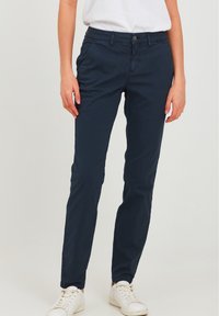 Mørkeblå slim-fit bukser laget av bomull, med sidelommer, knappelukking foran og en jevn tekstur. Kombinert med hvite sneakers.