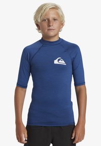 Blå, kortärmad rash guard med rund halsringning och vit logotypdetalj. Tillverkad av elastiskt material med en texturerad yta.