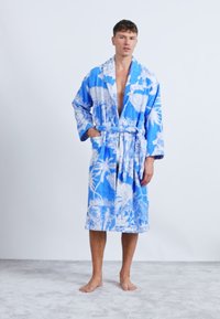 Roupa azul feita de tecido suave, com padrões florais brancos e de palmeiras, com mangas largas e um cinto amarrado na cintura.