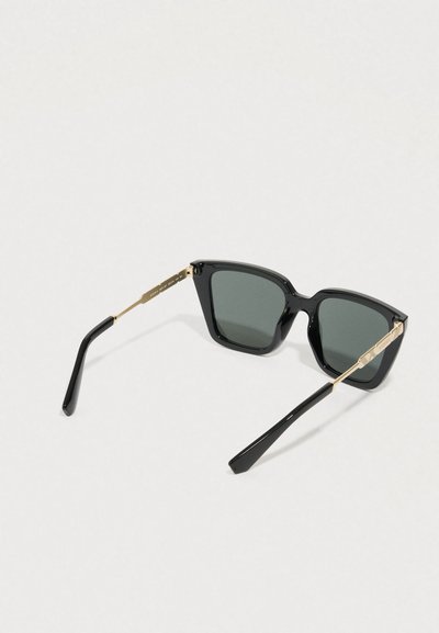 Czarne okulary przeciwsłoneczne z geometryczną oprawką, szarymi soczewkami oraz złotymi metalowymi ozdobami na zawiasach i końcówkach zauszników. Gładkie, błyszczące wykończenie.