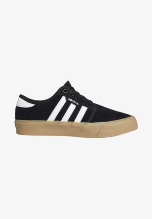 Czarny zamszowy sneaker z białymi paskami, okrągłym noskiem, sznurowanym przodem i gumową podeszwą. Na boku znajduje się logo marki.