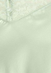 Lichtgroene satijnen top met kantdetails, voorzien van een V-hals en kleine knopen. Soepele textuur met een delicate, geprinte kantafwerking.