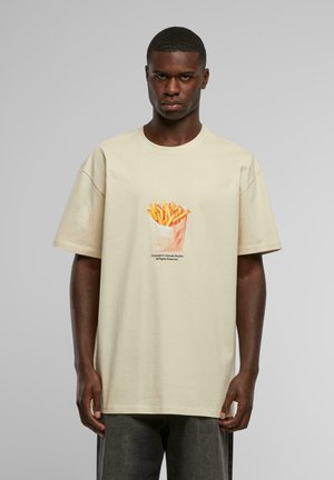 Beige short-sleeve t-shirt featuring a colorful graphic of French fries in a paper container, with text below the design.