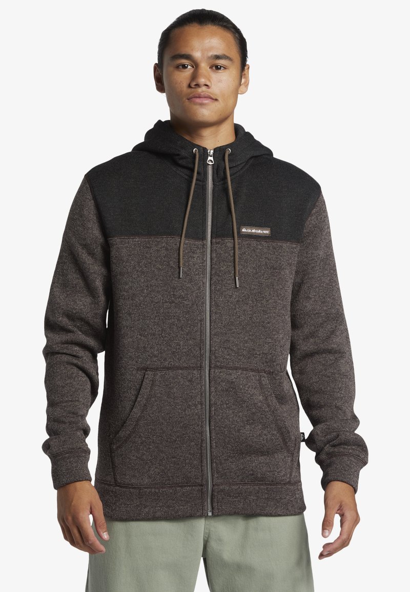 Men's zip-up hoodie in dark brown and black, featuring a textured fabric and a drawstring hood, with front pockets and a logo patch.
