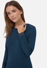 Camiseta de manga larga en color navy de tejido suave, con detalles de encaje en los hombros y puños, un escote redondeado y un diseño ajustado.