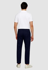 Pantaloni navy con una vestibilità dritta e due tasche posteriori, abbinati a una polo bianca maniche corte e sneakers di colore chiaro.
