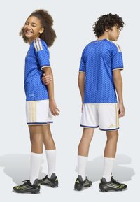 Blue soccer jersey with a patterned design, gold stripes, white shorts, and integrated white socks; features black cleats with neon accents.