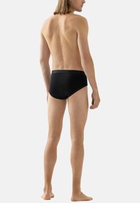 Slip neri di tipo brief con finitura liscia e vita bassa, indossati da una persona con pelle chiara e capelli castani di lunghezza media.