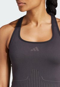 Canotta sportiva nera con scollo arrotondato, dotata di un sottile logo Adidas e strisce verticali texturizzate lungo la parte anteriore.