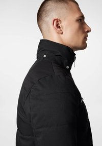 Czarna pikowana kurtka z wysokim kołnierzem, z zatrzaskami i gładką fakturą. Widok z boku podkreśla zorganizowany design i dopasowanie.