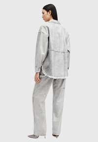 Conjunto de chaqueta y pantalones de mezclilla gris, con dobladillo deshilachado, ajuste relajado y costuras en contraste. Los accesorios incluyen zapatos de tacón alto brillantes.