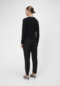 Haut noir à manches longues avec un col rond, associé à un pantalon noir à rayures et des sandales à talons ouverts noires.