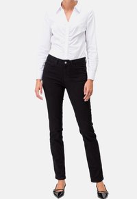 Černé úzké džíny vyrobené z denimu, s klasickým pětipocket designem a minimálním kovovým vybavením. V pairu s bílou košilí na knoflíky.