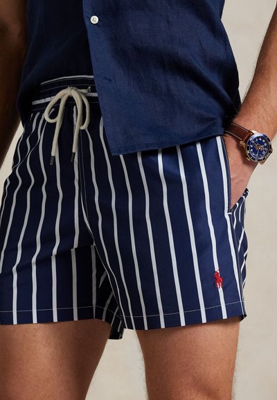 Calções de banho azuis-marinho com riscas verticais brancas, cintura elástica, cordão, bolsos laterais e um pequeno detalhe de logótipo vermelho.