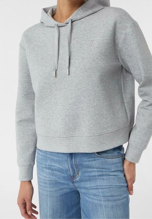 Person iført en lysegrå cropped hættetrøje med snore og lyseblå jeans, vist fra midt på brystet til hoften mod en hvid baggrund.