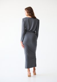 Robe ajustée à manches longues en tissu jersey gris, dotée d'un col rond et d'une coupe longue jusqu'au sol, avec des détails froncés à l'arrière.