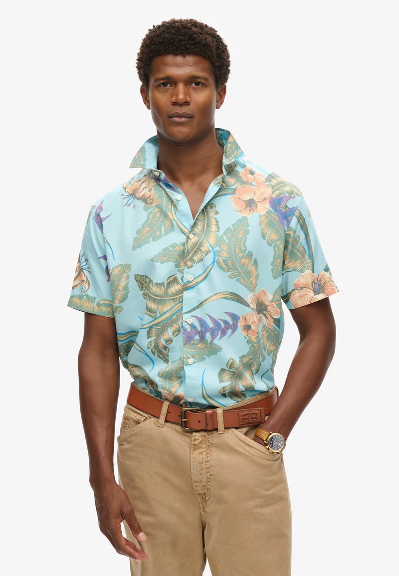 Camicia hawaiana a maniche corte, di colore azzurro chiaro, con stampa floreale. Presenta un colletto con bottoni ed è realizzata in tessuto leggero.