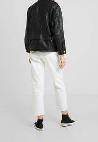 Černá kožená bunda s uvolněným střihem, opatřená zadní sponou a bočními kapsami, doplněná bílými zkrácenými kalhotami a černými kotníkovými teniskami.