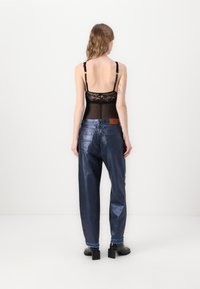 Body de encaje negro con tirantes ajustables, combinado con unos vaqueros oscuros de tiro ancho y brillante y botas de tobillo de tacón cuadrado negras.