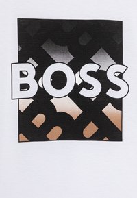 T-shirt blanc avec un grand carré noir à motif dégradé, affichant le mot "BOSS" en lettres blanches en gras, centré à l'intérieur.