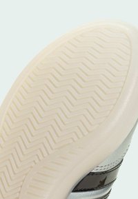 Gummisula på sko med fiskbensmönster, med en slät, rundad kant och kontrasterande svarta och silverfärgade ränder på ovandelen.