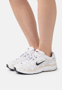 Sneaker Nike P-6000 bianchi e beige in materiali mesh e pelle, con logo Swoosh nero, suola robusta e un sistema di allacciatura dettagliato.