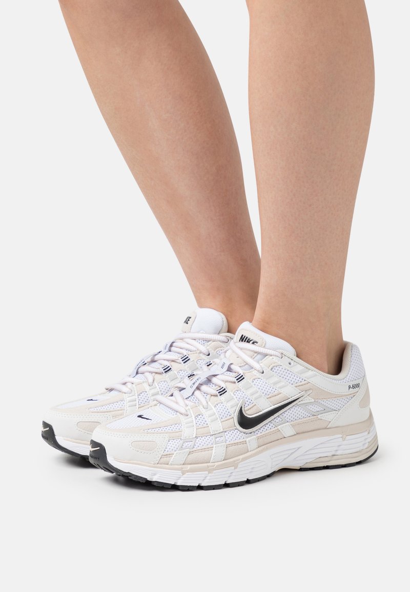 Sneaker Nike P-6000 bianchi e beige in materiali mesh e pelle, con logo Swoosh nero, suola robusta e un sistema di allacciatura dettagliato.