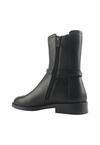 Bottines en cuir noir avec une fermeture éclair sur le côté, texture lisse, bout rond et petit talon carré. Détail de sangle simple au-dessus de la fermeture éclair.
