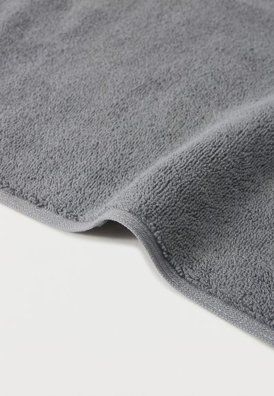 Απαλή γκρι πετσέτα από περκάλι με υφή από θηλιές, εμφανιζόμενη διπλωμένη απαλά πάνω σε λευκή επιφάνεια.