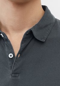 Polo shirt gris foncé avec un col, présentant une patte de boutonnage et une petite découpe. Le matériau semble doux avec une texture lisse.