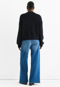 Maglione nero a coste con spalle scese, abbinato a jeans a gamba larga blu chiaro con tasche posteriori e taglio dritto.