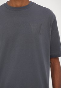 Gray cotton t-shirt with short sleeves, crew neck, and a subtle tonal logo on the left chest. Smooth texture and relaxed fit.