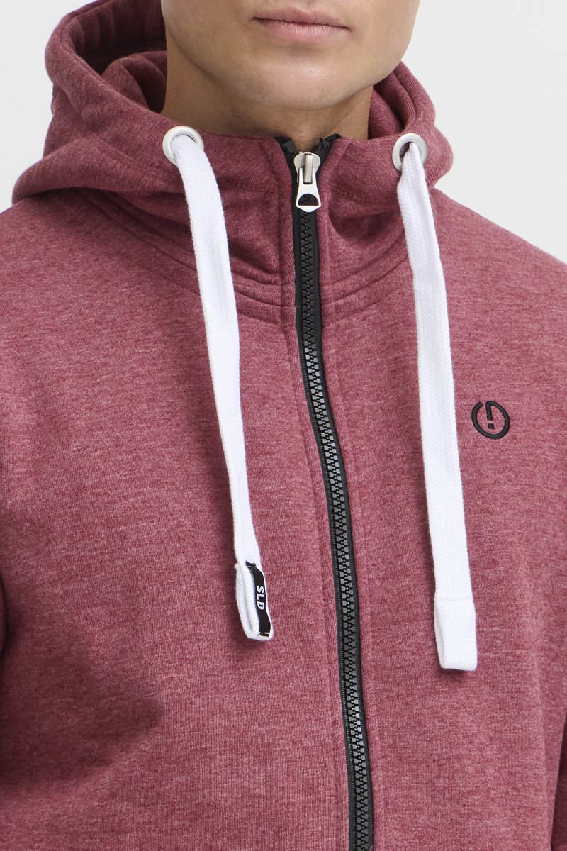 Bordowy hoodie na zamek z wysokim kołnierzem, białymi sznurkami, czarnym zamkiem i małym logo na klatce piersiowej. Miękka faktura materiału.