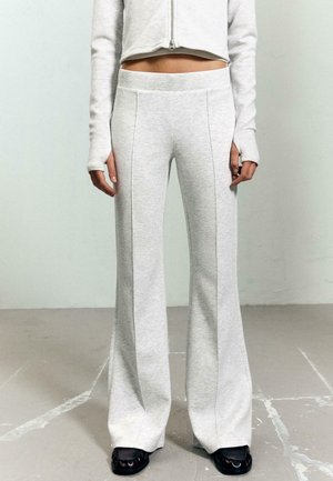 Sivé teplákové nohavice z mäkkej tkaniny, s vysokým pásom, širokým strihom nôh a viditeľnými bočnými švami. Kombinované s tmavými, plochými topánkami.