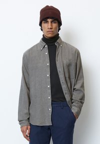 Gray button-up shirt with a subtle texture, worn over a black turtleneck. Features a chest pocket and a relaxed fit. Brown knitted beanie.
