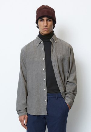 Gray button-up shirt with a subtle texture, worn over a black turtleneck. Features a chest pocket and a relaxed fit. Brown knitted beanie.
